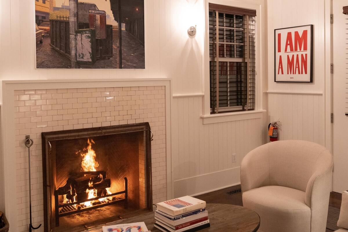 A cozy living room with a fireplace, a comfortable armchair, and a coffee table with books.