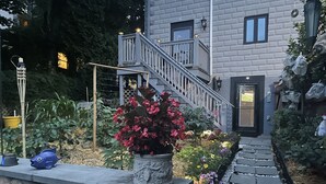 Ein gepflasterter Weg führt zu einem Haus mit einer Holztreppe und einer Tür.