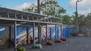 Un espace extérieur abrité, doté d’une série de portes bleues, dont certaines sont décorées d’œuvres d’art, et d’un sol en gravier parsemé de petites plantes.