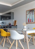 A modern dining area with a glass table, wooden chairs, and a painting of surfboards on the wall.