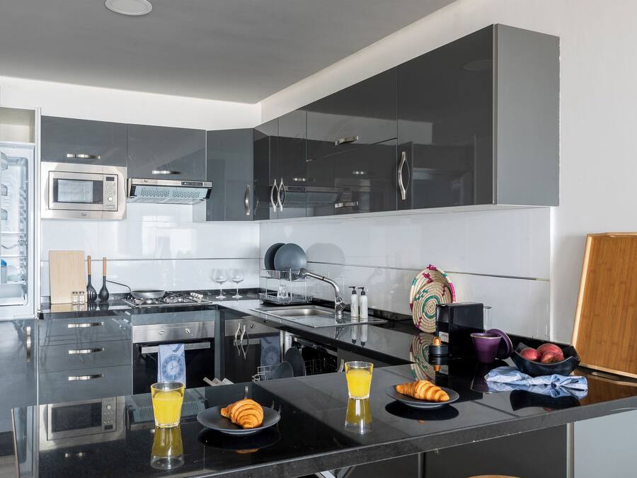 Una cocina moderna con horno empotrado, microondas y estufa. Hay un desayuno preparado con croissants, jugo y un bol de fruta.
