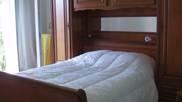 Cama com cabeceira de madeira e espelho acima.