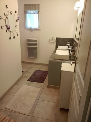 Casa de banho compacta com lavatório, espelho e porta-toalhas. Uma janela com cortinas é visível, e um pequeno aquecedor está fixado na parede.