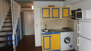 A compact kitchen with yellow and blue cabinets, a washing machine, a microwave, and a sink. - Mezzanine À LA Marina (Saint-François)