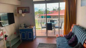 A living room with a sofa, a TV, a small cabinet, and a balcony with a table and chairs. - Mezzanine À LA Marina (Saint-François)