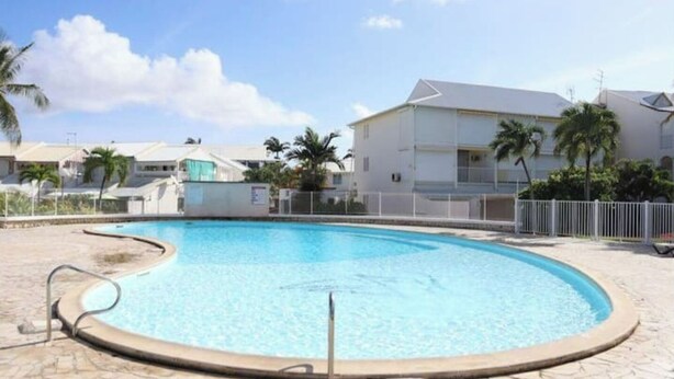 A swimming pool with a curved edge, surrounded by a paved area and a white fence. - Mezzanine À LA Marina (Saint-François)