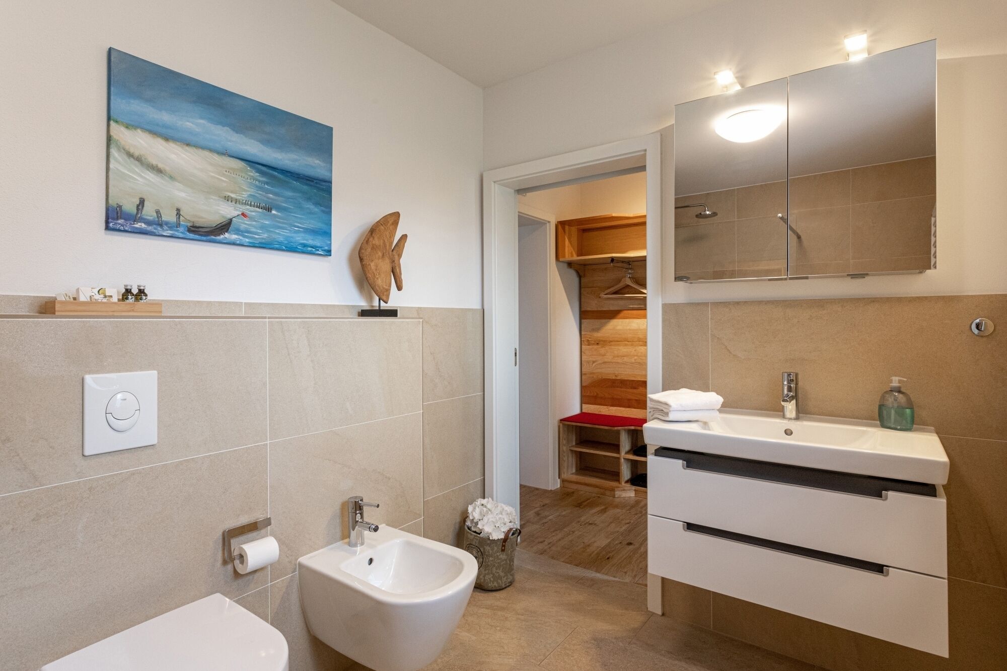 Ein modernes Badezimmer mit einem Bidet, einem Waschbecken und einem Spiegel. An der Wand hängt ein Gemälde und es steht eine Holzskulptur dort.