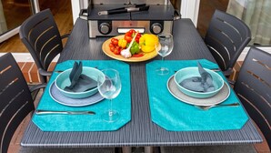 Una mesa de comedor con dos sillas, una parrilla portátil y un plato de verduras.