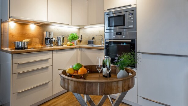 Una cocina moderna con armarios blancos, electrodomésticos de acero inoxidable y un bol de frutas de madera sobre la encimera.