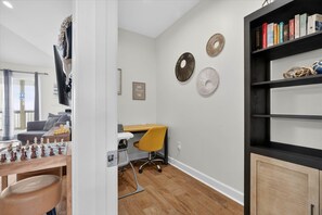 Una habitación con un tablero de ajedrez, un escritorio con una silla y una estantería llena de libros.