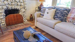 Una sala de estar acogedora con chimenea de piedra, un sofá blanco con cojines estampados y una mesa de centro de madera rústica.
