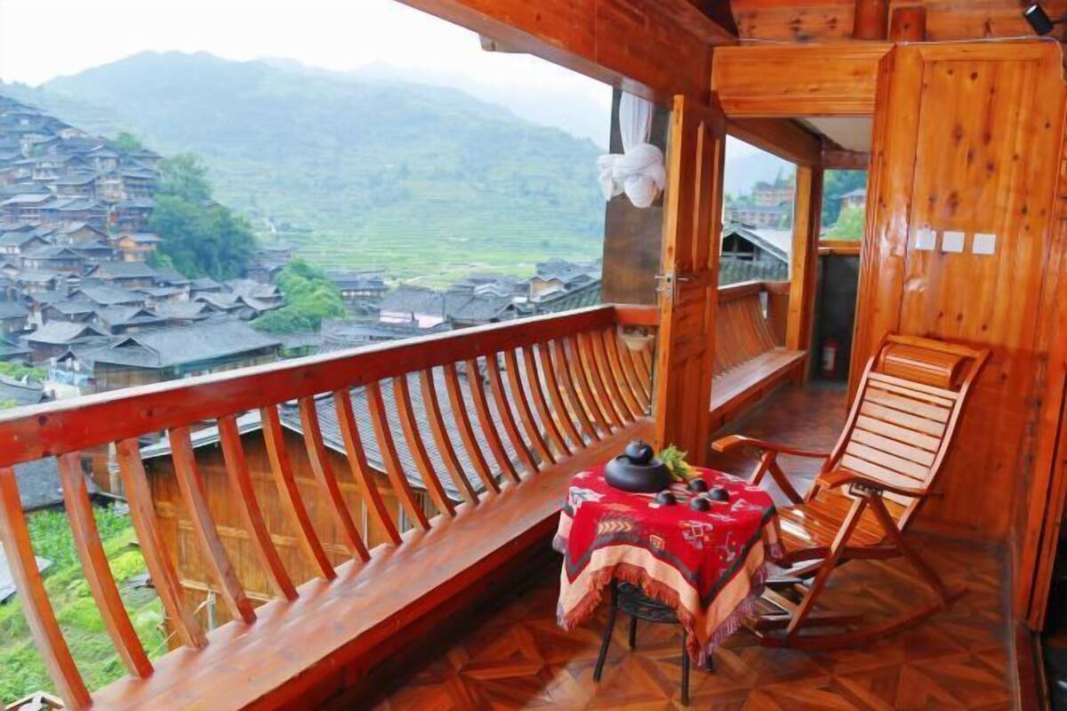 Un balcón de madera con una mesa y sillas, con vistas a un pueblo y montañas.