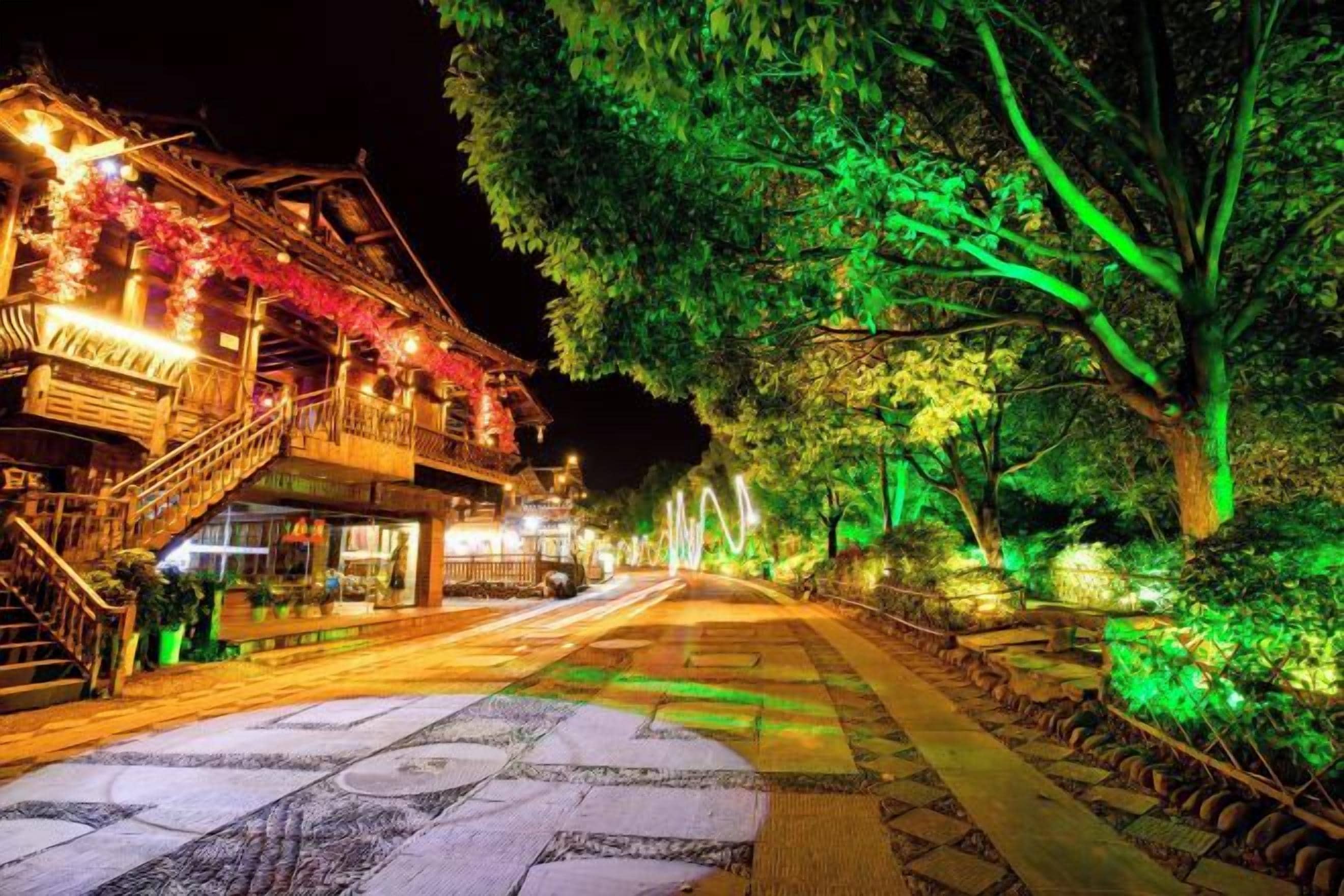 Une scène de rue nocturne avec des bâtiments et des arbres illuminés.