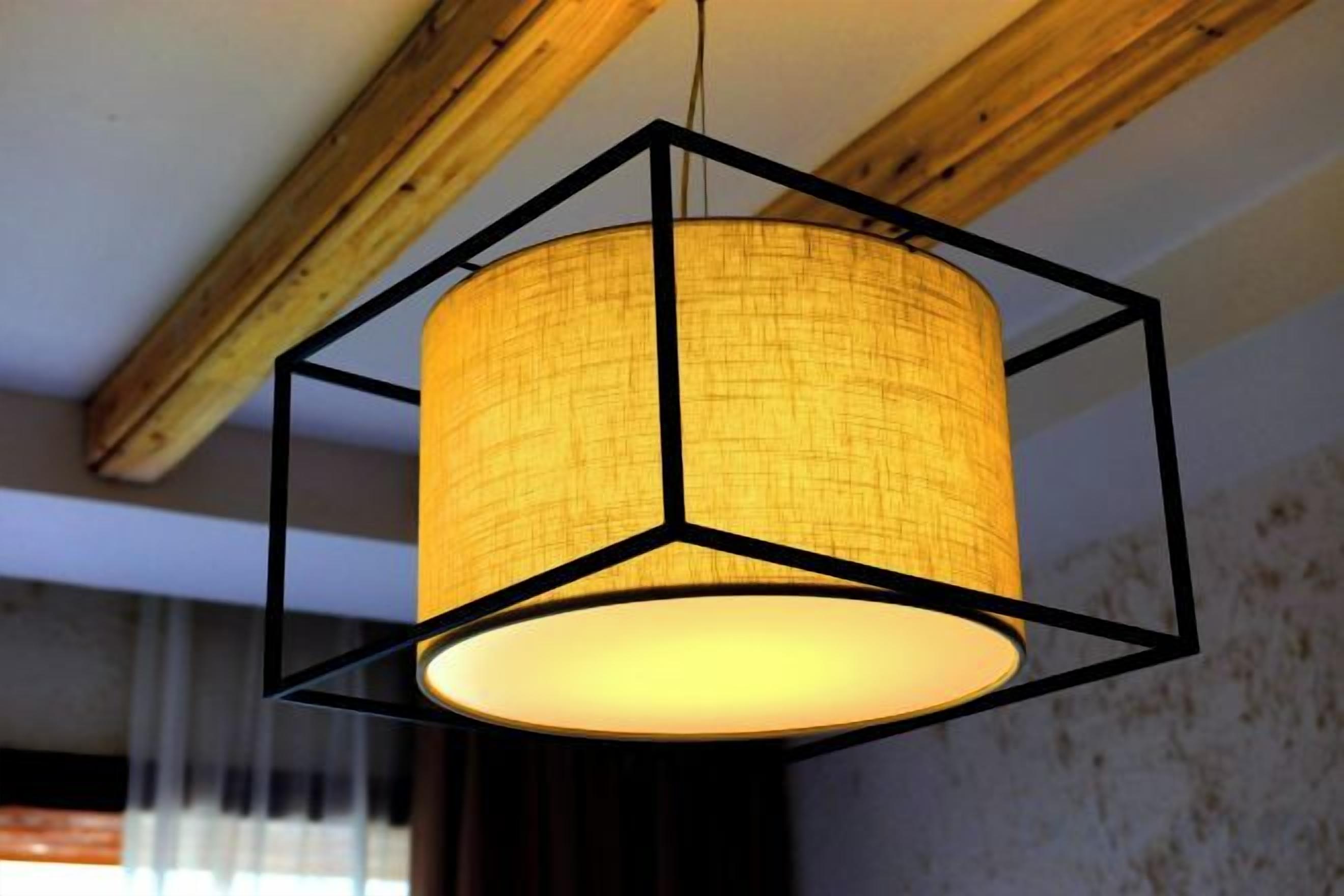 A hexagonal pendant light fixture with a cylindrical shade hanging from a wooden ceiling beam.
