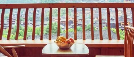 A balcony with a wooden railing, a small table with a bowl of fruit, and a view of traditional buildings in the background.