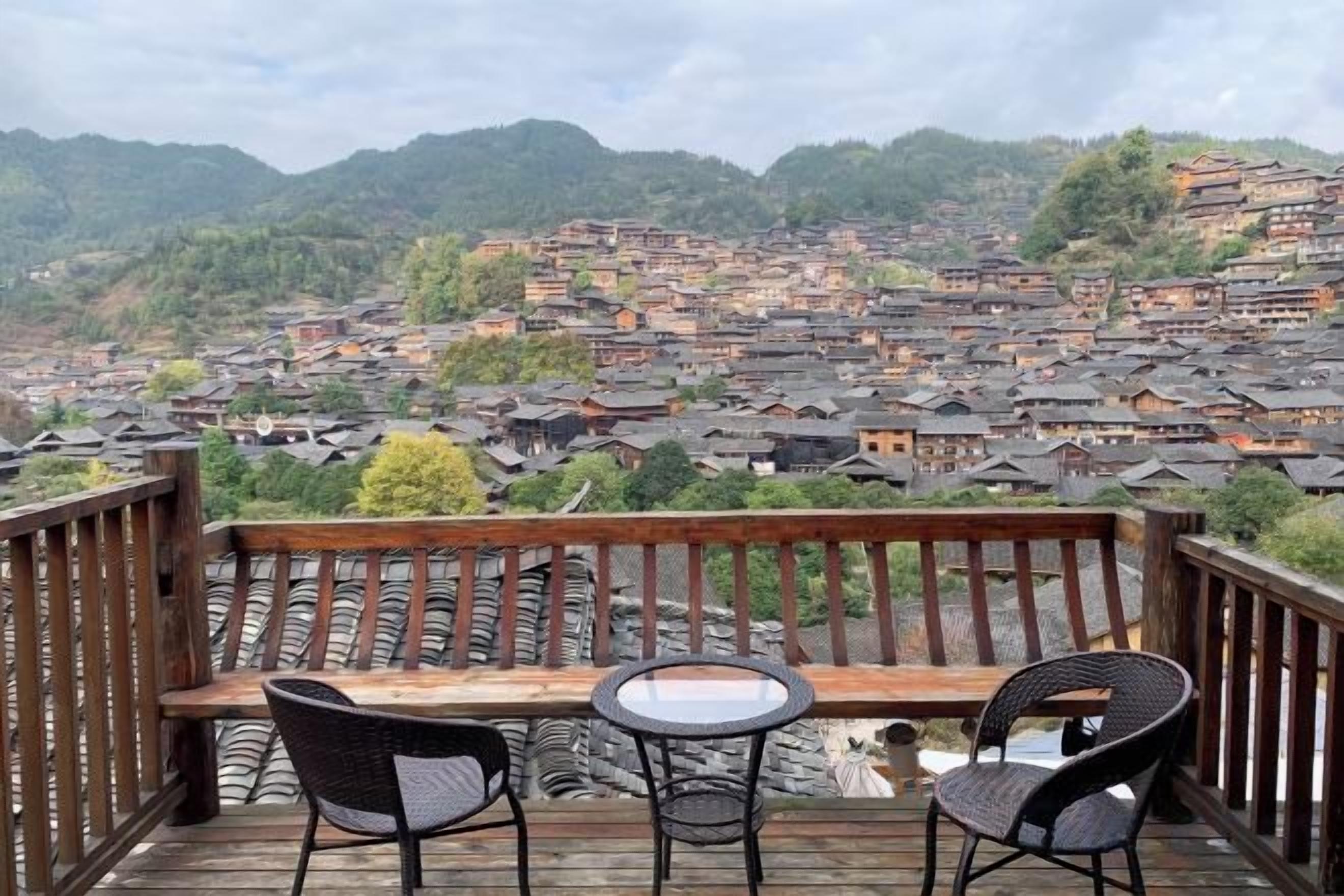 Eine Holzterrasse mit zwei Stühlen und einem Tisch, mit Blick auf ein Dorf mit traditioneller Bebauung.
