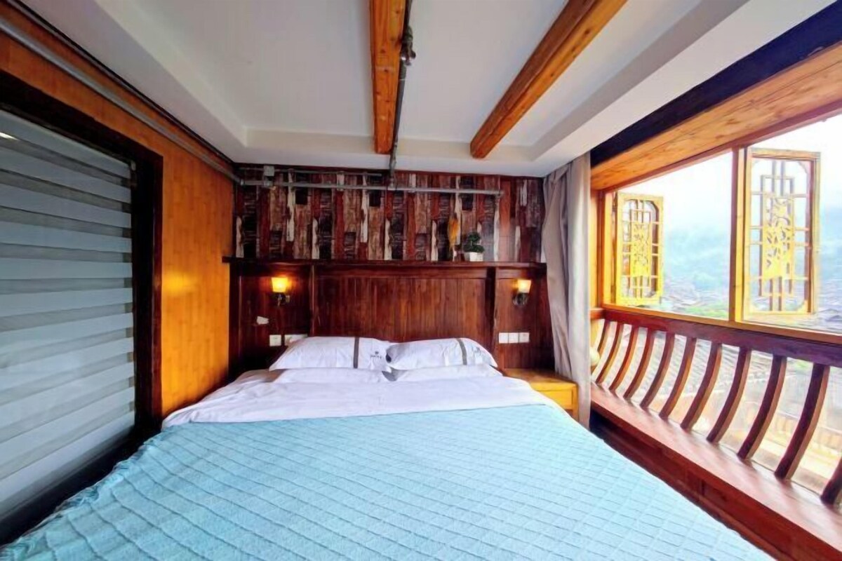 Quarto com cabeceira de madeira, cama com roupa de cama branca e janela com vista para o exterior.