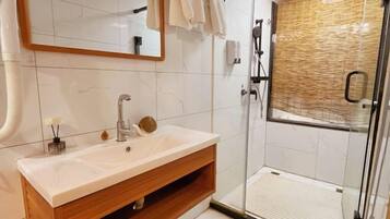 A modern bathroom with a white sink, wooden vanity, a glass shower enclosure, and a mirror with a wooden frame.