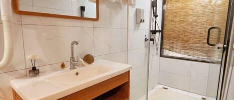 A modern bathroom with a white sink, wooden vanity, a glass shower enclosure, and a mirror with a wooden frame.