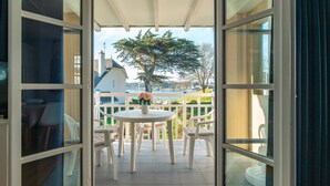 An open balcony with a table and chairs, a potted plant, and a view of the surrounding area. - Côté Ouest - Appt avec piscine partagée (Benodet)