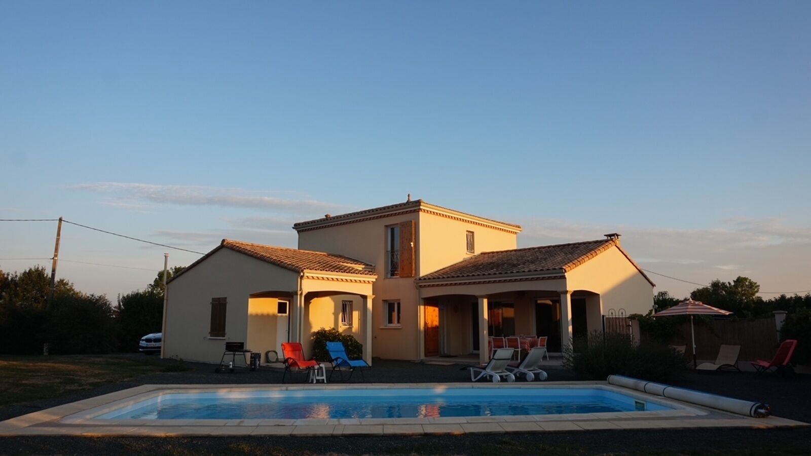 A two-story house with a swimming pool, outdoor seating, and a clear sky.
