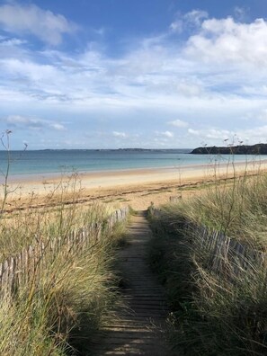 Un sendero de madera que conduce a una playa con cielos despejados y tierras lejanas.