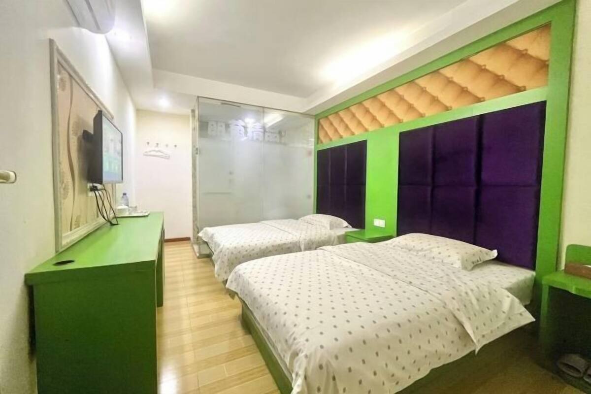 A hotel room with two beds, a green desk, a mirror, and a television.