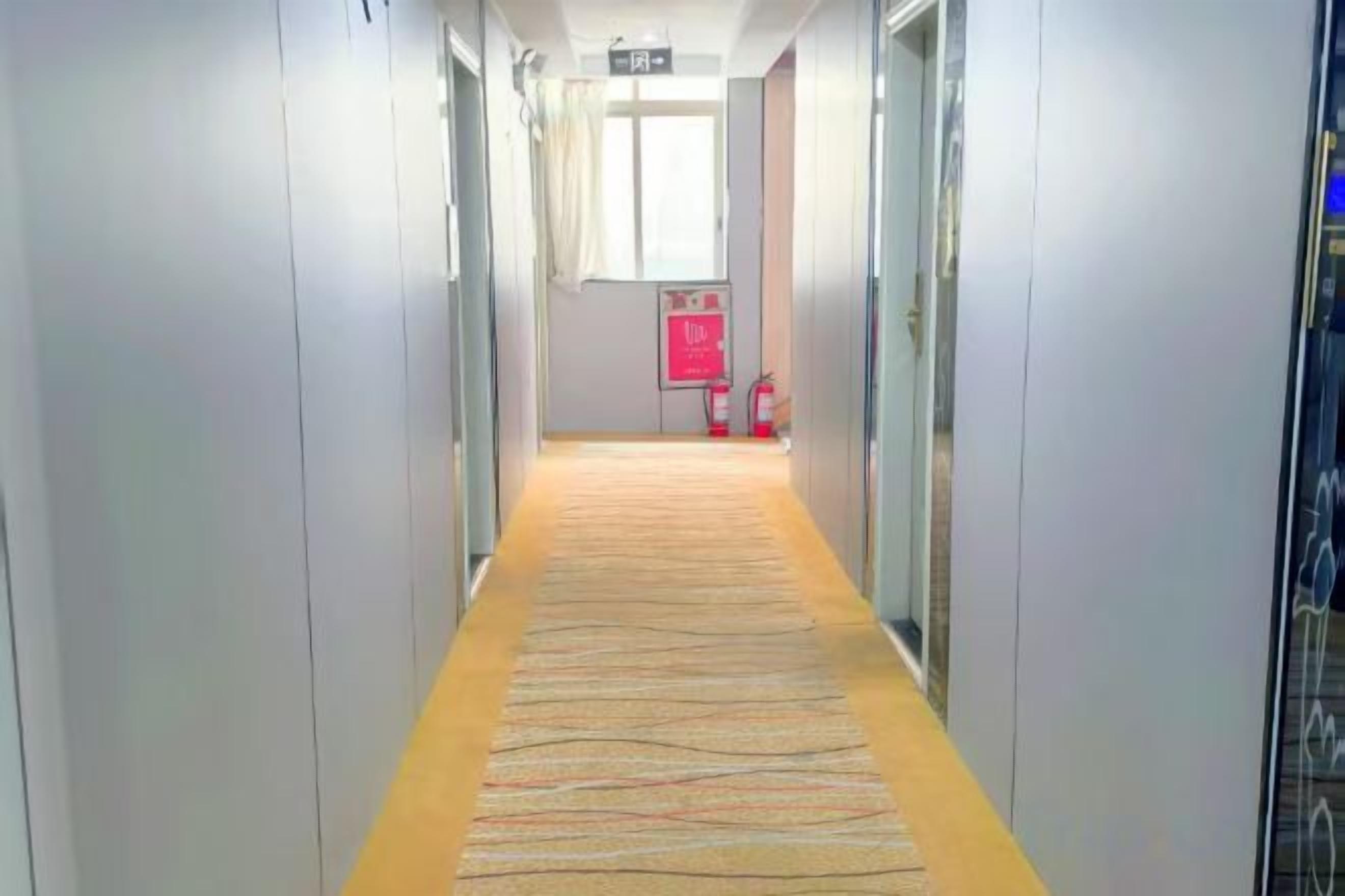A hotel corridor with a carpeted floor, glass doors, and a fire extinguisher on the wall.