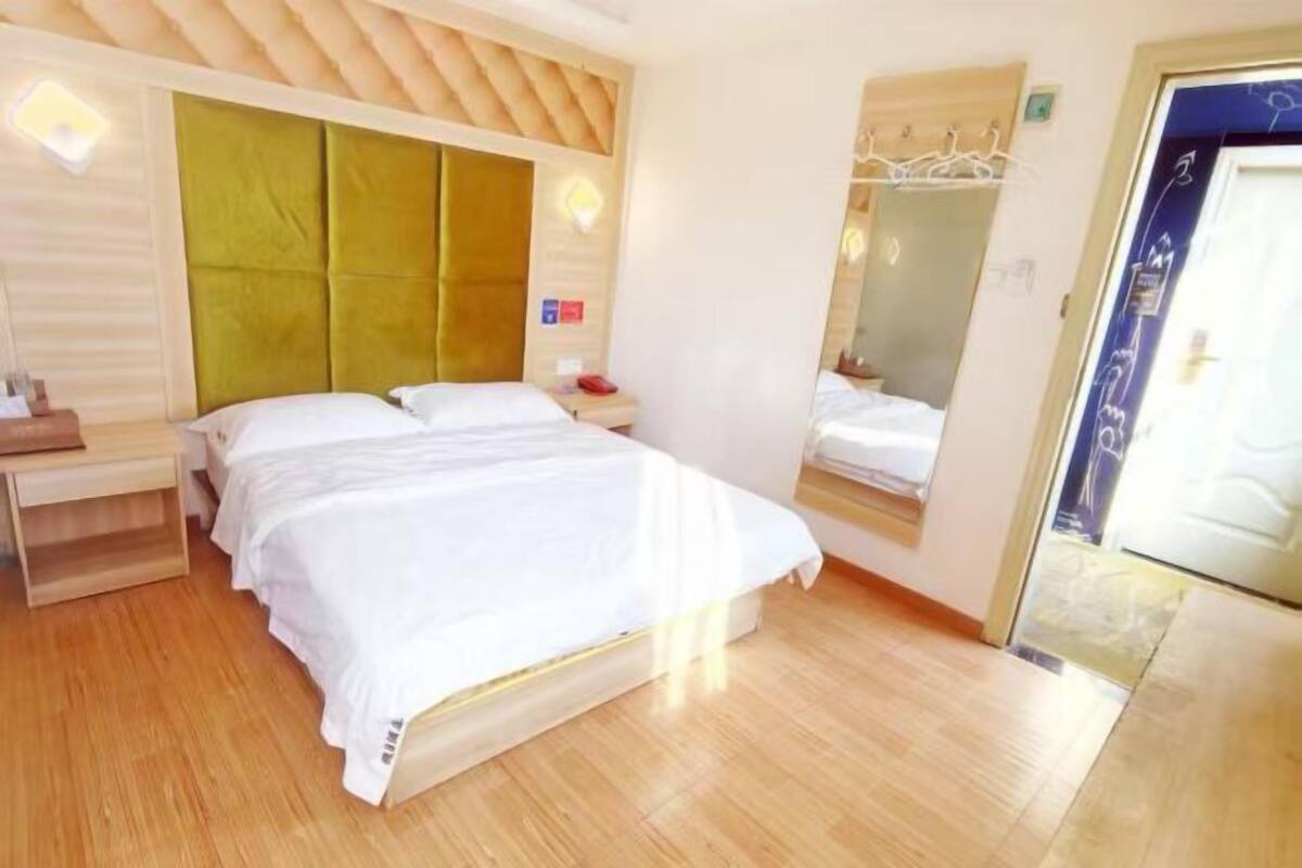 A hotel room with a bed, bedside table, and a mirror.