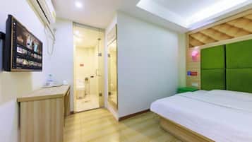 A hotel room with a bed, a desk, a shower area, and a mounted TV.