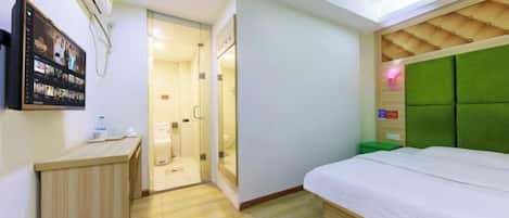 A hotel room with a bed, a desk, a shower area, and a mounted TV.
