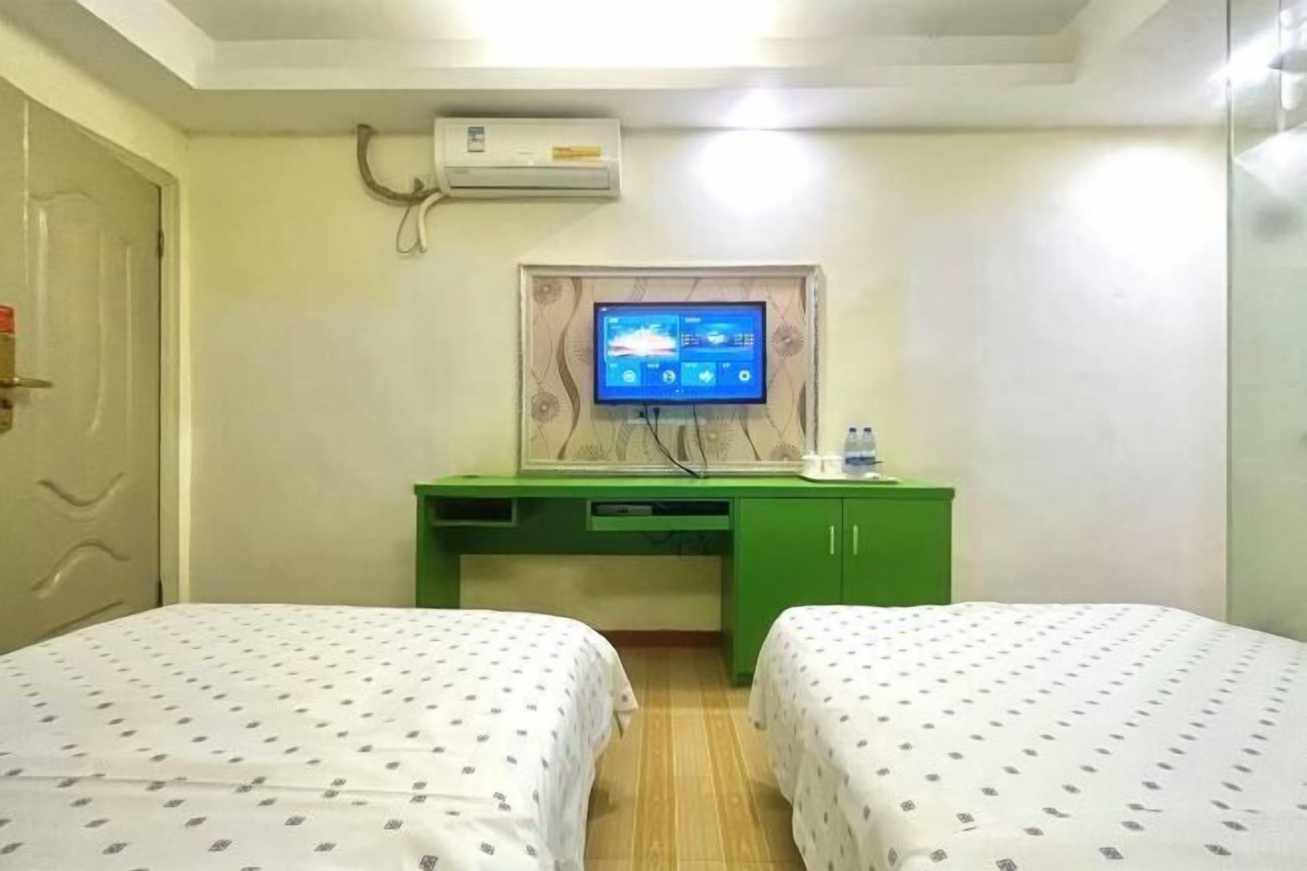 A hotel room with two beds, a desk with a computer monitor, and an air conditioning unit.
