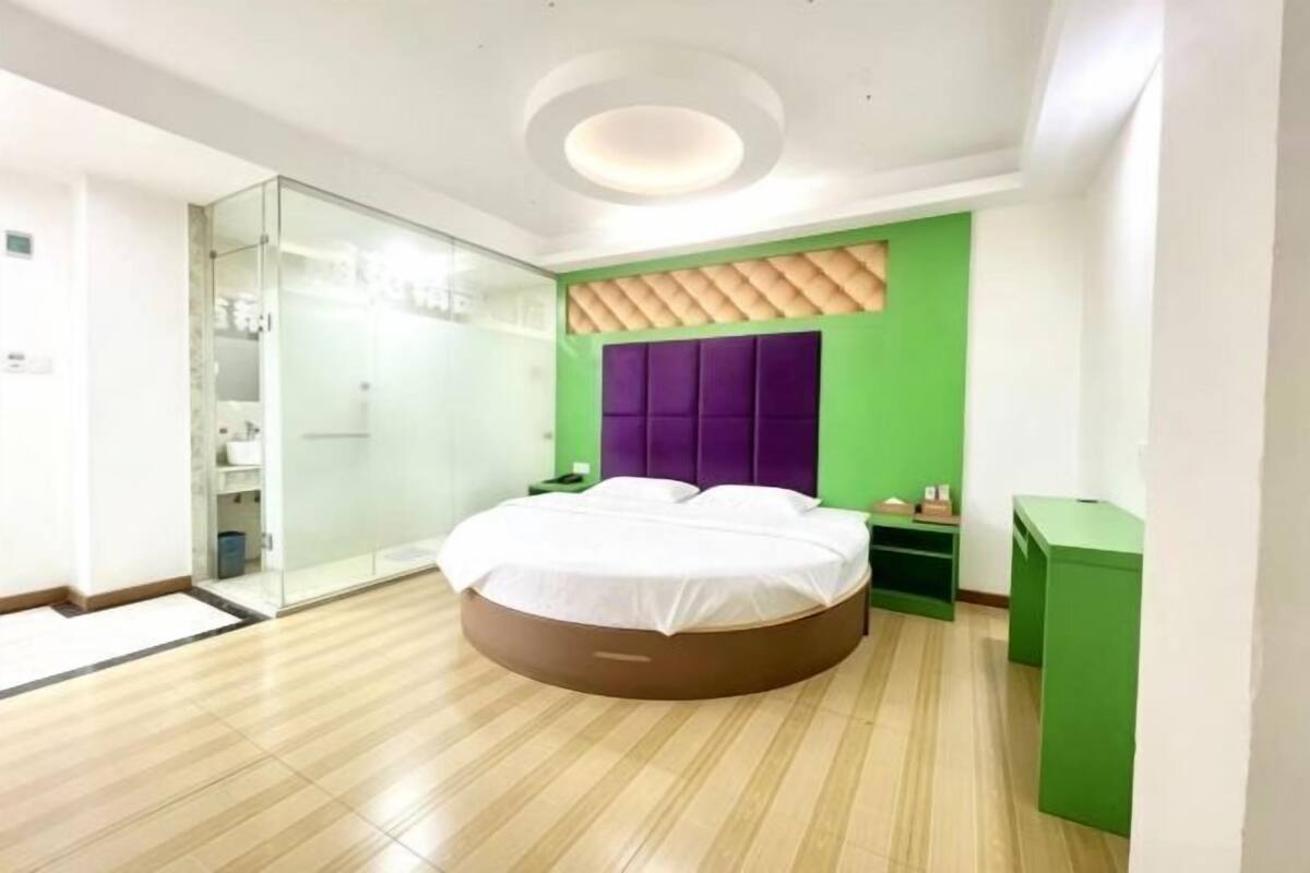 A modern bedroom with a round bed, a glass shower enclosure, and a green accent wall.