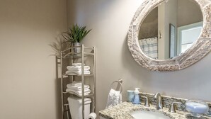 Un baño con inodoro, toallero con toallas dobladas, lavabo con encimera de mármol, espejo y planta en maceta.