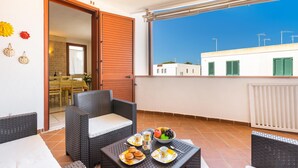 A balcony with wicker furniture, a table with breakfast items, and a view of buildings and a clear sky. - 3193 Appartamento Vittoria by Barbarhouse (Nardò)