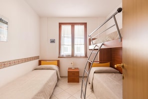 Ein kleiner, gut beleuchteter Raum mit zwei Einzelbetten, einem hölzernen Nachttisch, einer Leiter und einem Fenster mit Vorhängen.