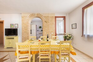 Enjoy meals in this dining area with a long table set for four, featuring comfortable chairs and a brick archway leading to the kitchen.