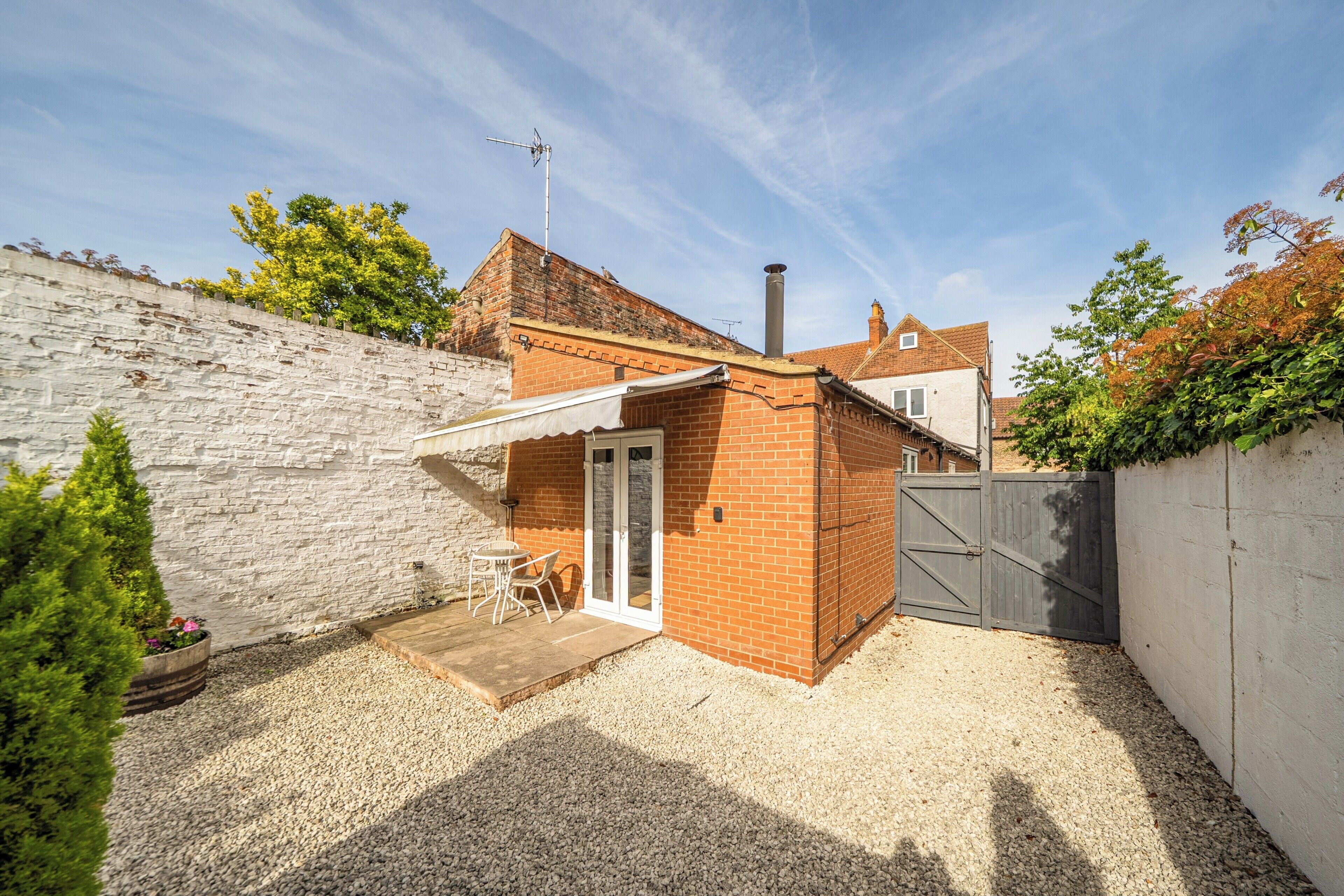 A brick house with a white exterior, a small patio with a table and chairs, and a gravel driveway.