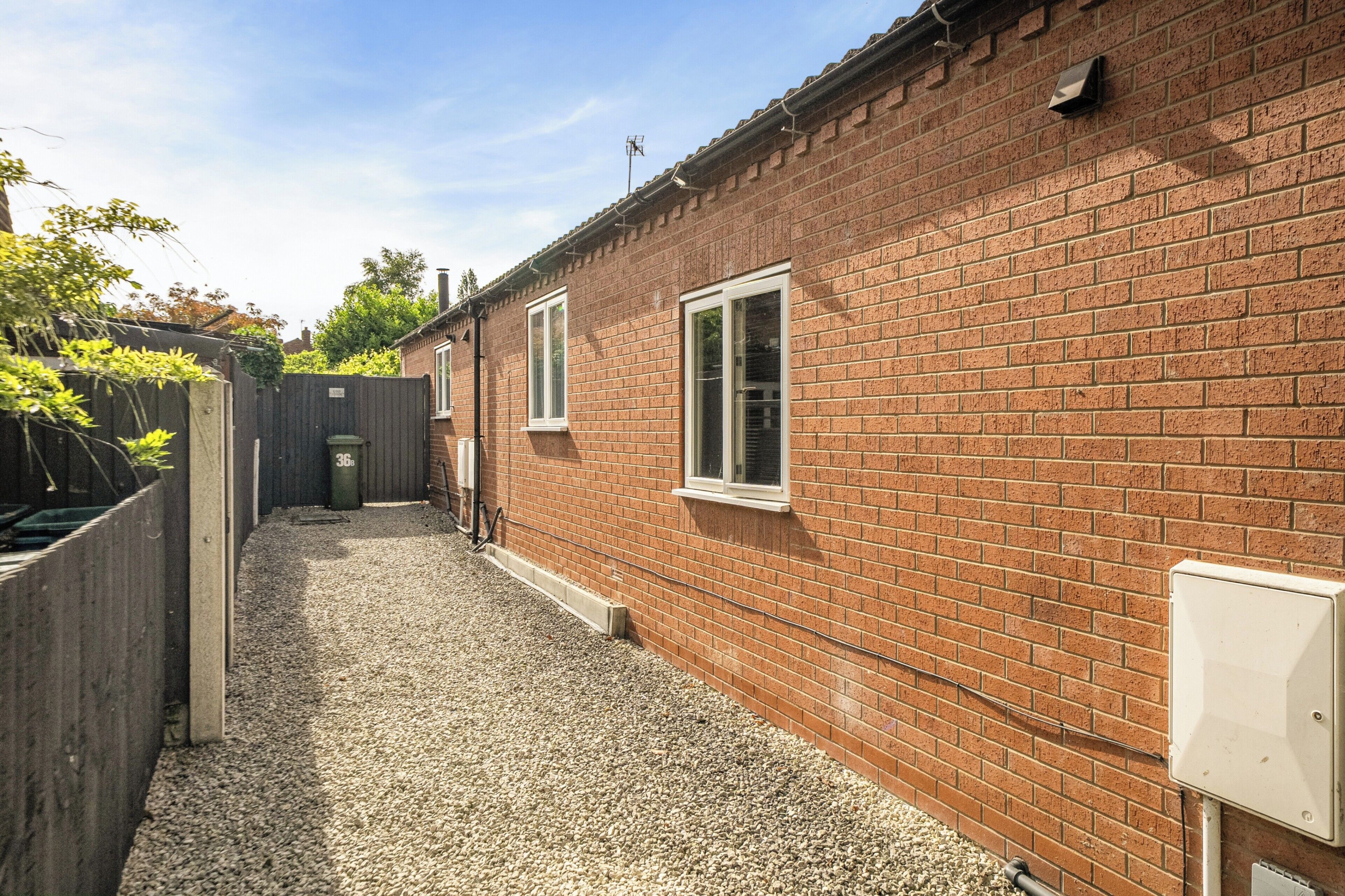 A narrow gravel path leading to a brick building with two windows and a white electrical box.