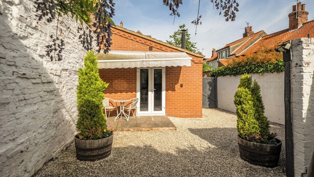 A courtyard with a brick house, white walls, and a gravel ground. There are two potted plants and a table with chairs. - Cozy Lodge Sleeps 4 in Barton-upon-humber (Barton-upon-Humber)