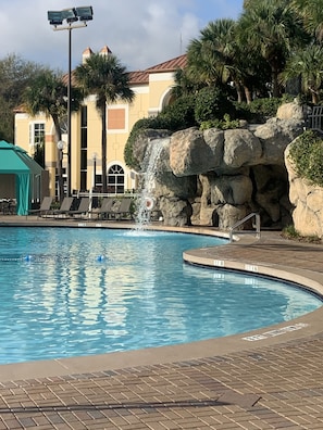 Ein Pool mit Wasserfall, Liegestühle und ein Gebäude mit einem Kachelziegeldach im Hintergrund.