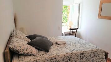 Um quarto com cama, almofadas, mesa de cabeceira, abajur e uma cadeira.