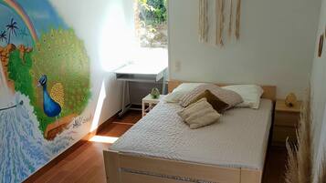 Un dormitorio con cama, un mural en la pared, una mesita y una ventana.
