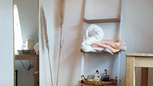 A room with a wooden floor, a mirror, a vase with dried plants, a shelf with towels, and a table. - Aux Chambres du Chadoux de Chateaubourg (Chateaubourg)