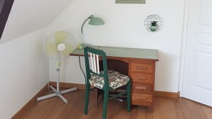 A room with a wooden desk, a green chair, a standing fan, and a small table with a clock. - Aux Chambres du Chadoux de Chateaubourg (Chateaubourg)