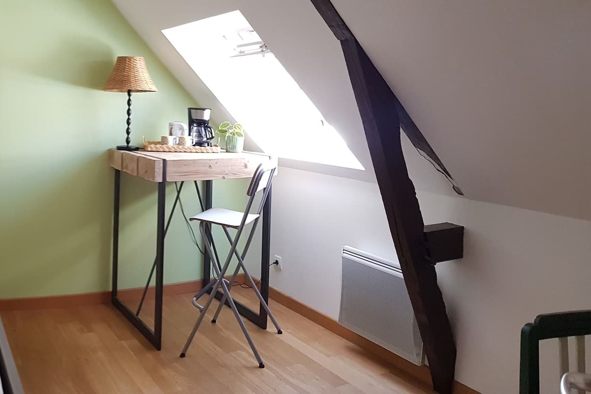A bedroom with a bed, a desk, and a chair. There is a window providing natural light.