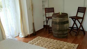 A bedroom with a bed, a wooden barrel, two chairs, a woven rug, and a tall plant.