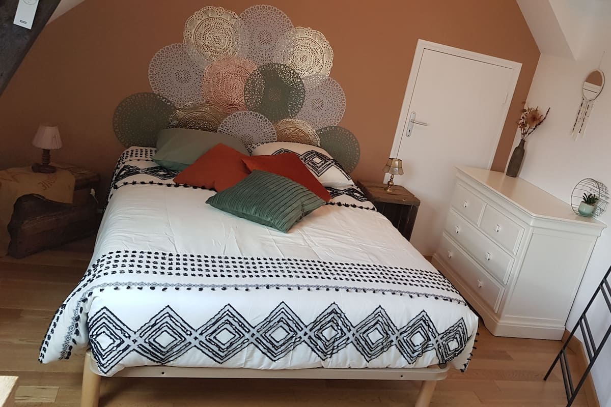 A bedroom with a bed, a dresser, a nightstand, a lamp, and a ladder.