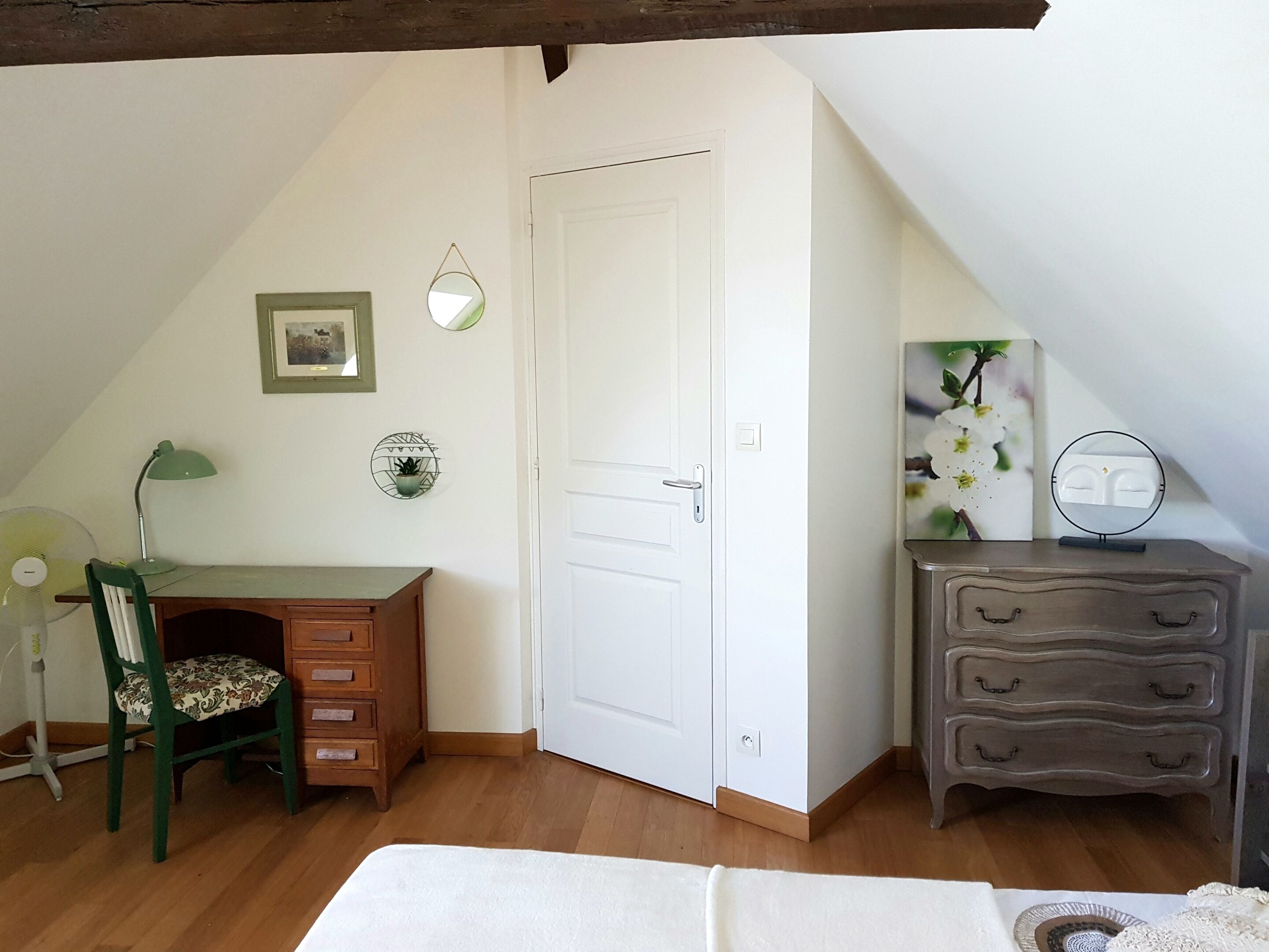 Un dormitorio con un escritorio de madera, una silla, un aparador, una cama y una puerta.