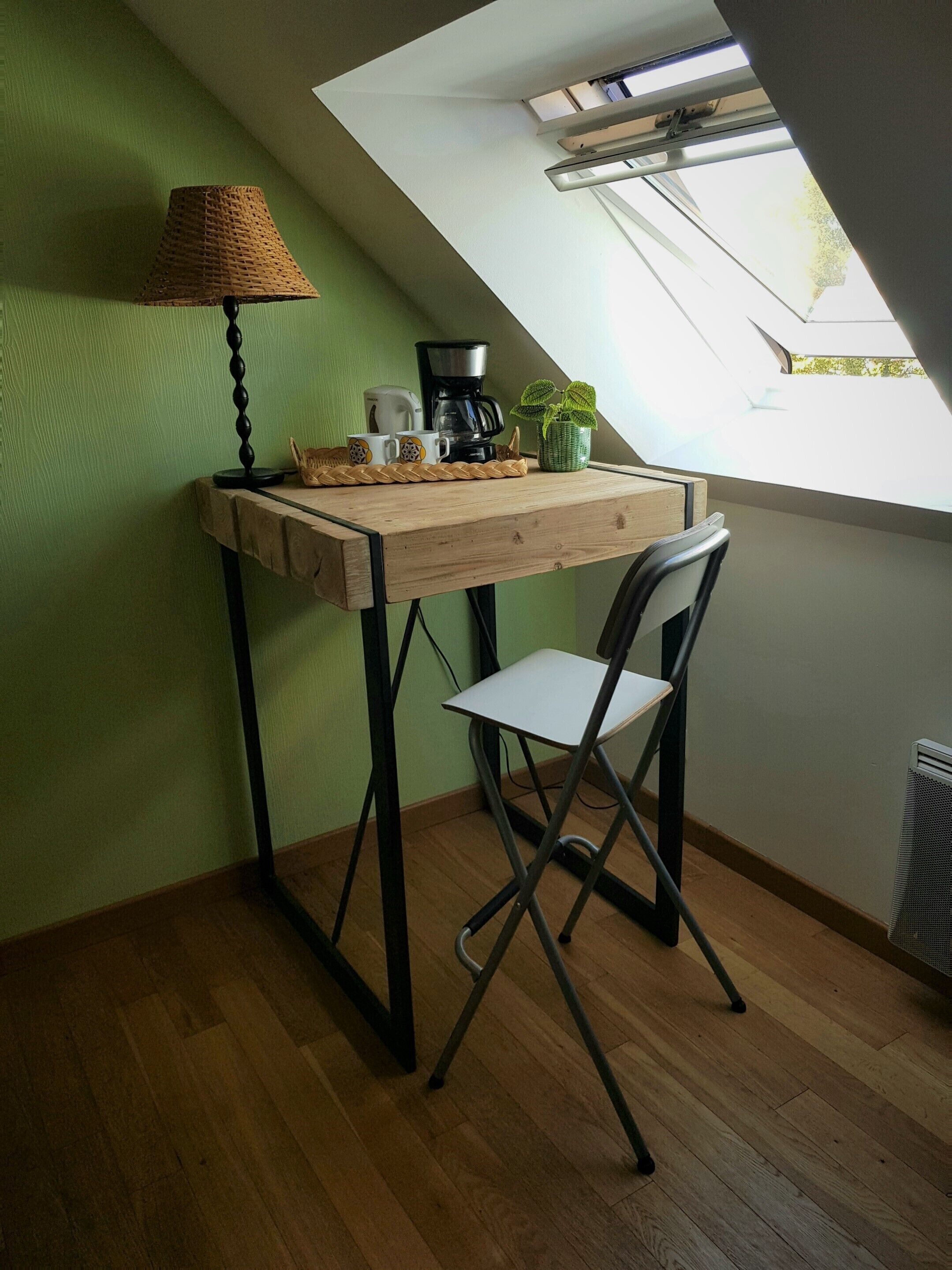 Una habitación pequeña y acogedora con un escritorio de madera, una silla, una lámpara, una cafetera y una planta en maceta.